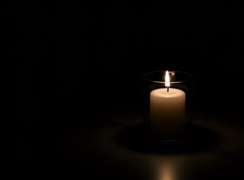 A lit candle in a glass holder against a dark background
