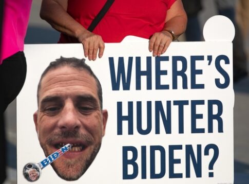 A protestor holding a sign with a large image of a mans face and the text WHERES HUNTER BIDEN?