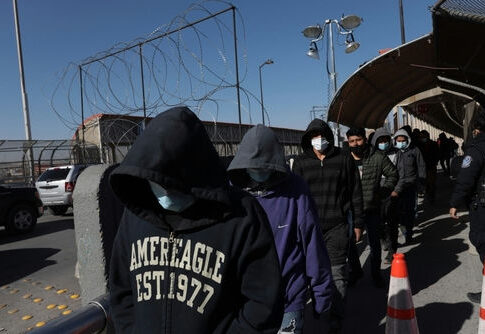 People in hoodies and masks walking beside a fence.